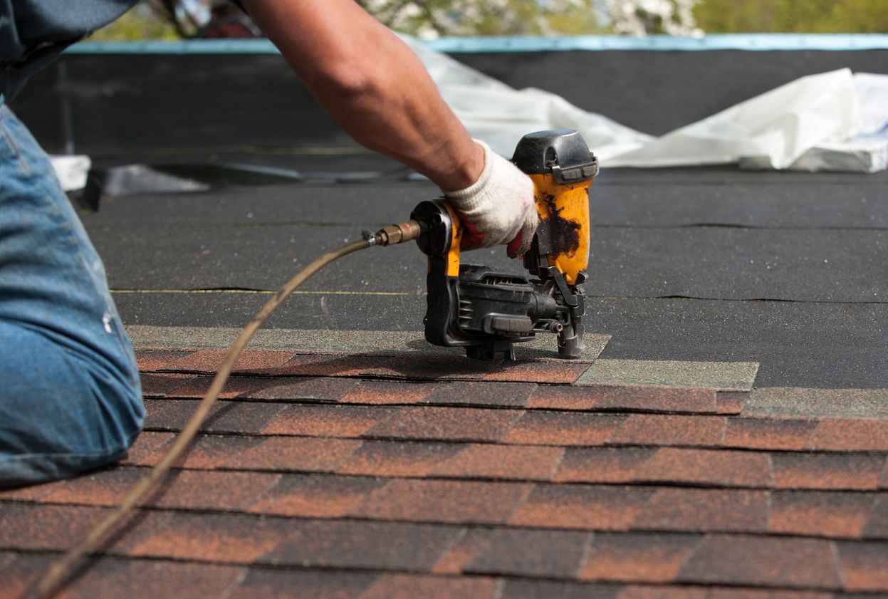 Roofer nailing architectural shingles with a pneumatic nailer