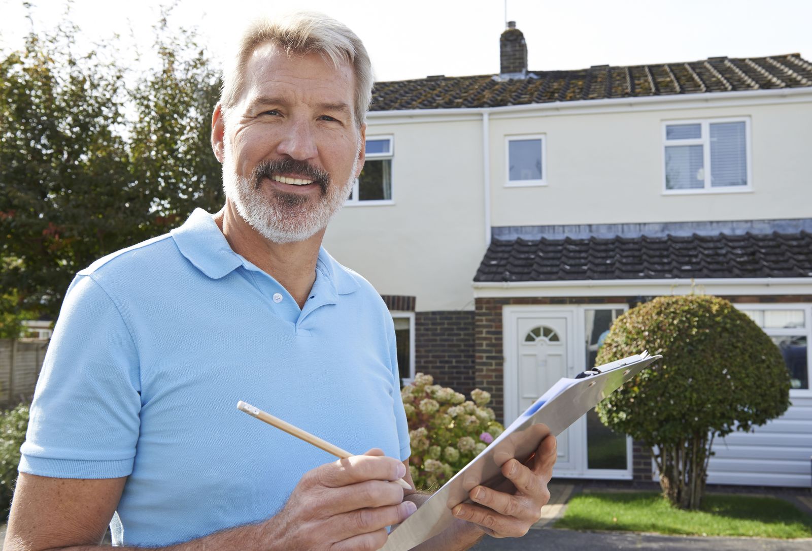 Contractor in a polo shirt holding a clipboard in front of a house
